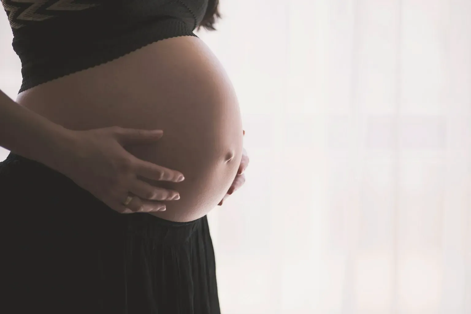 Close-up of a pregnant belly with a hand resting on it