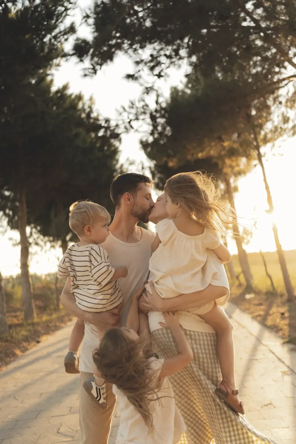 Parents sharing a kiss while carrying their children on a sunny path