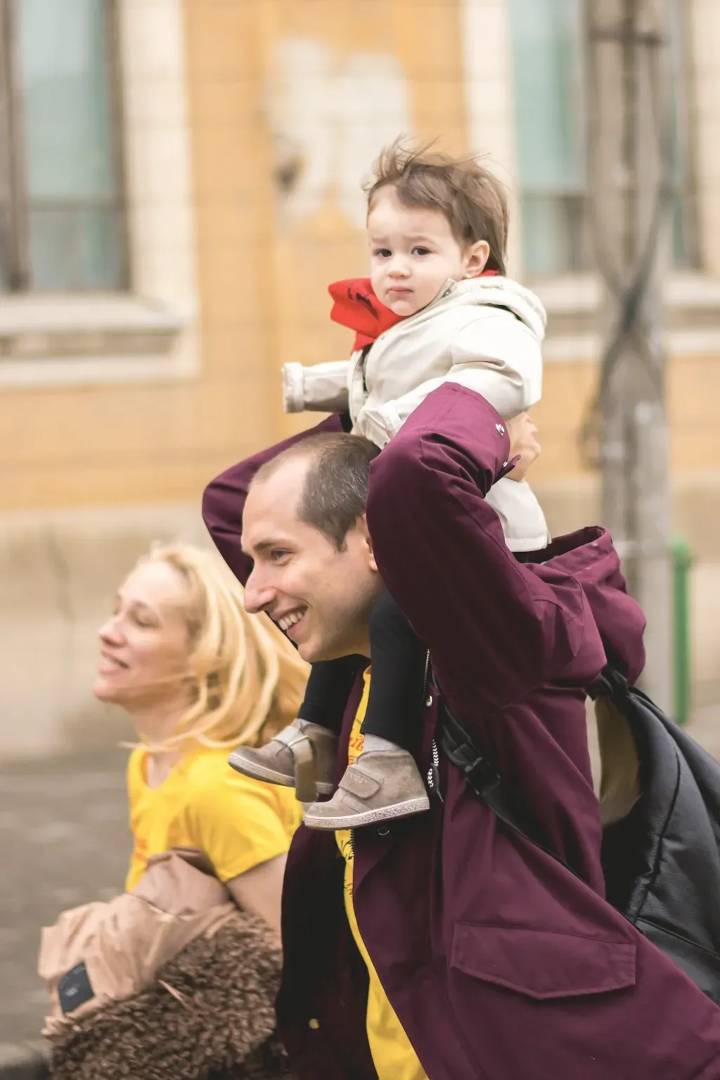 A father carrying a toddler on his shoulders beside the mother outdoors