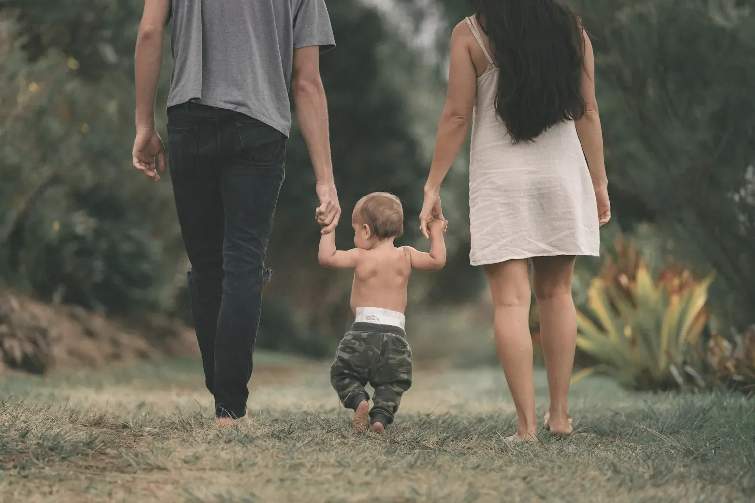 Parents walking along a path, holding their toddler's hands