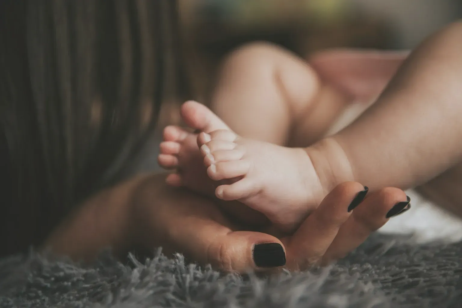 A mother's hand holding her baby's bare feet on a soft rug