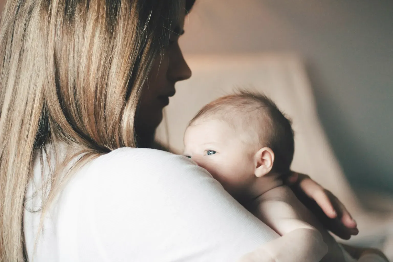 A mother holding her baby against her shoulder at home