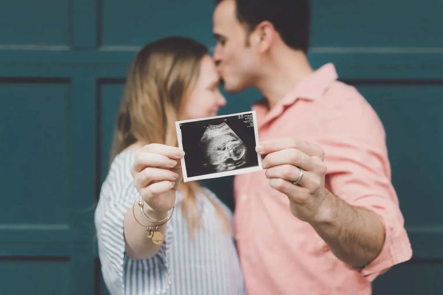 A couple holding up an ultrasound photo while sharing a kiss