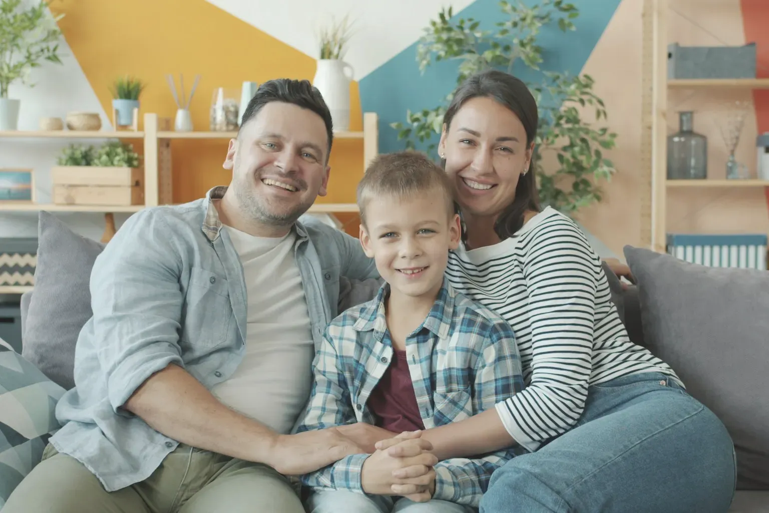 Parents and their son sitting together on a sofa in a colourful room