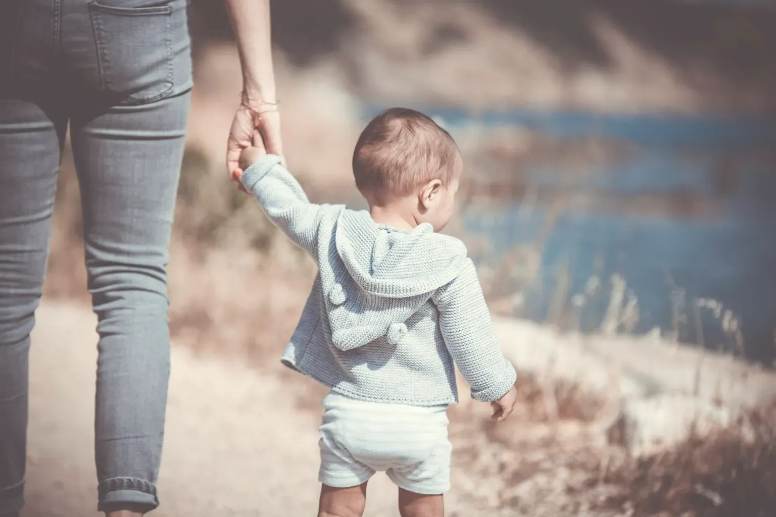 A toddler walking along a path, holding an adult's hand